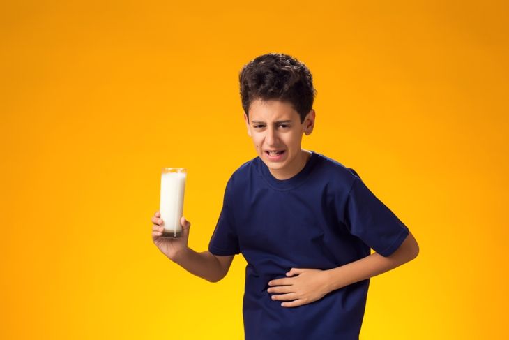 Dairy intolerant unhappy child boy holding glass of milk and feeling stomach pain