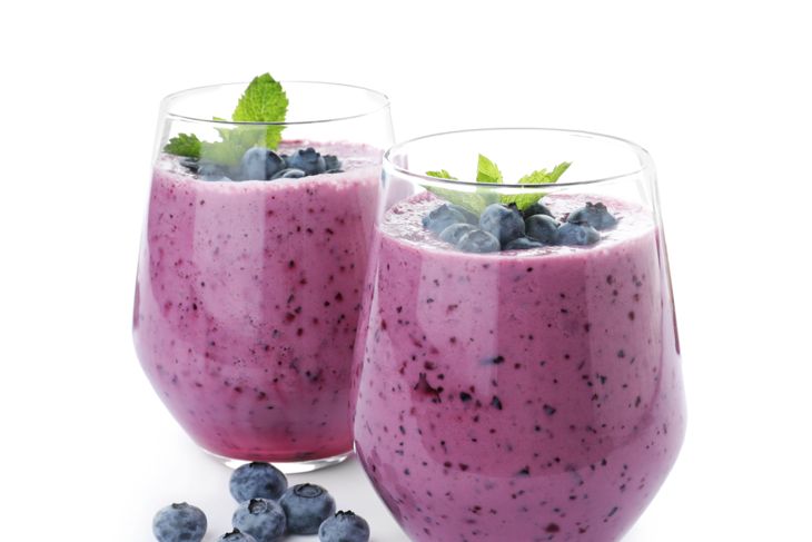 Two glasses of thick purple blueberry smoothies topped with whole blueberries and mint leaves, with fresh blueberries scattered nearby—representing a blueberry mint smoothie with a fizzy finish.