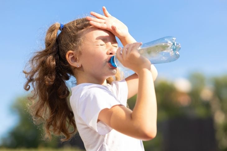 little girl drinking water from bottle in heat