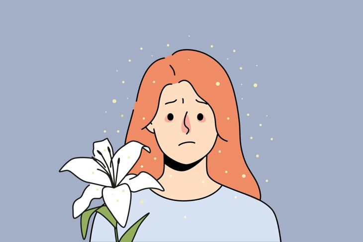 Illustration of a red-haired woman standing near a blooming white flower, surrounded by floating yellow pollen-like particles. Her eyes appear teary and her nose is red, suggesting sensitivity or discomfort related to seasonal changes or allergens.