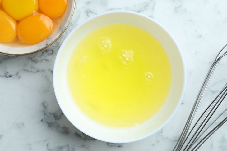 Egg whites, yolks and whisk on white marble table