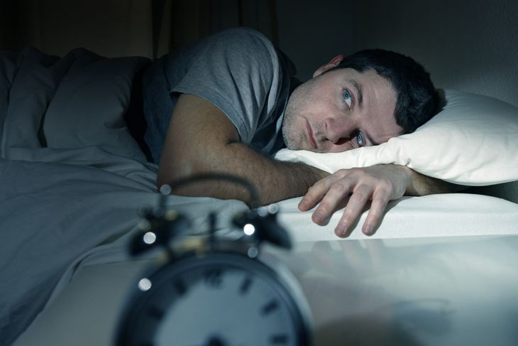 young man in bed with eyes opened suffering insomnia and sleep disorder thinking about his problem