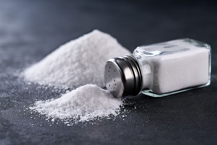 Salt shaker and pile of spilled salt crystals on a black table