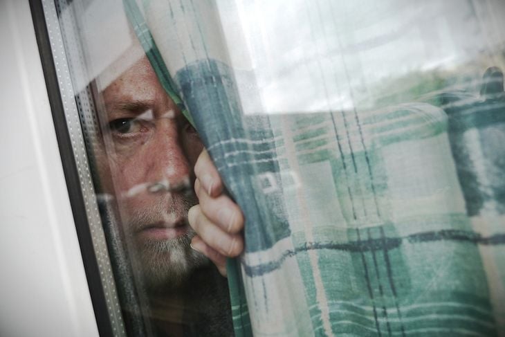 Anxious or suspicious man peeping through window from behind curtain 
