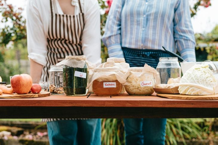 A couple of people standing next to a table with kombucha ingredients 