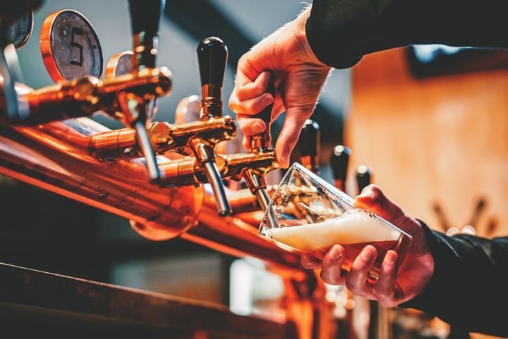 bartender hand at beer tap pouring a draught beer in glass serving in a bar or pub