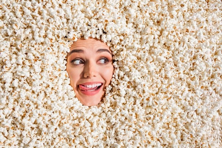 Photo of hungry dreamy young woman face showing stick out curious peeking hole covered tasty caramel popcorn