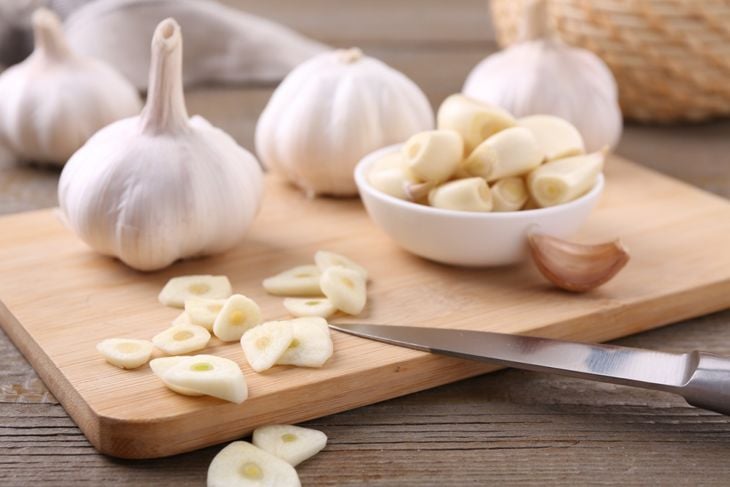 Aromatic cut garlic, cloves and bulbs on wooden table, closeup