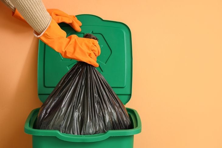 Woman taking garbage bag from trash bin near orange wall, closeup