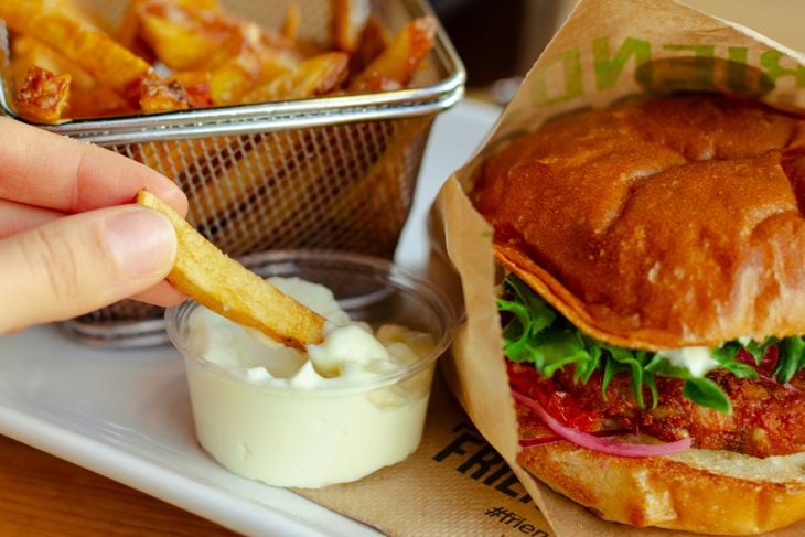 A person dipping french fries into mayo next to a hamburger