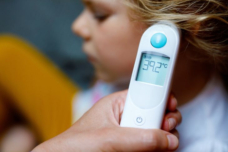 Mother takes temperature for her little preschool daughter, sick child with infrared in ear thermometer at home
