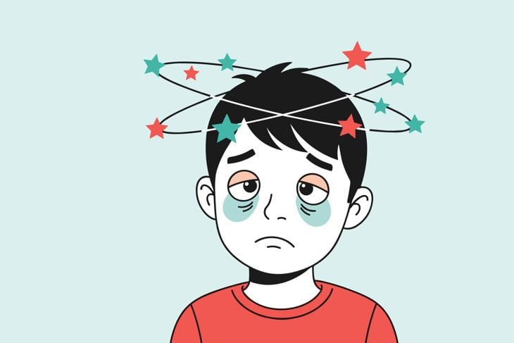Sick boy looking dizzy with colorful stars spinning around his head and dark circles under his eyes on a light background.