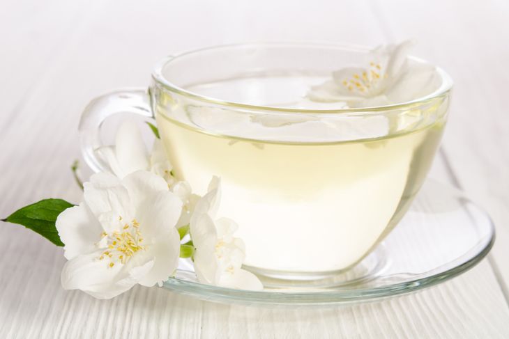 Glass cup of tea with jasmine on the white wooden background