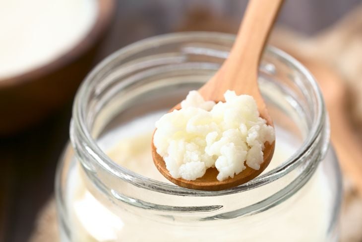 Milk kefir grains on wooden spoon on top of a jar of kefir, photographed with natural light