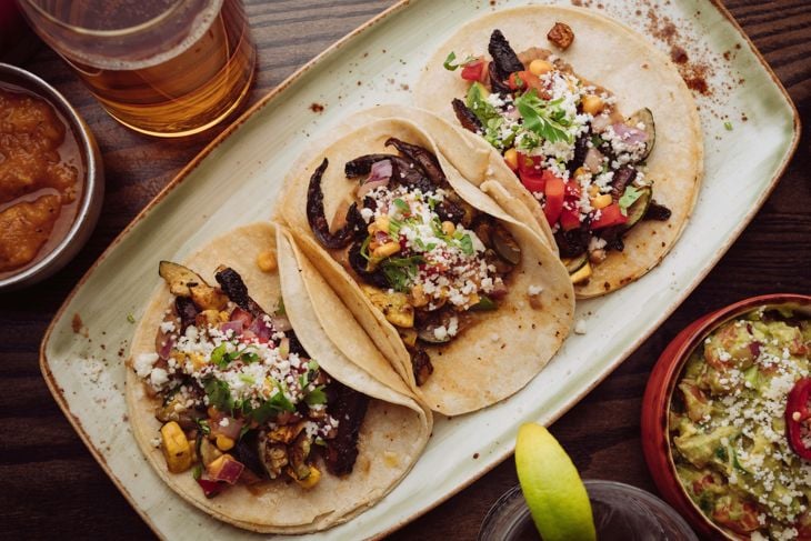 Three tacos are sitting on a plate next to a glass of beer photo