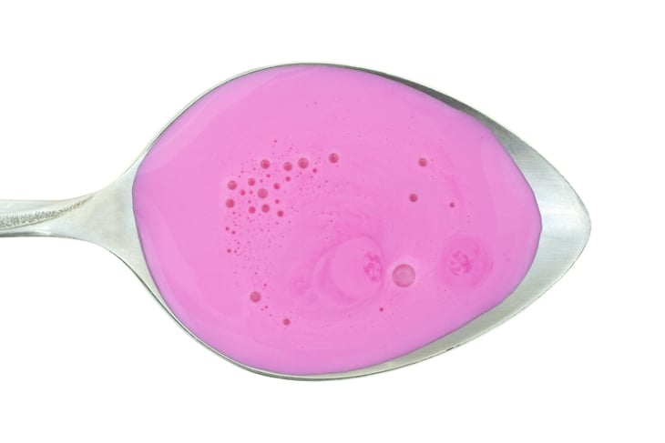 Top view of sour stomach and anti-diarrhea medicine on a metal spoon atop a white background