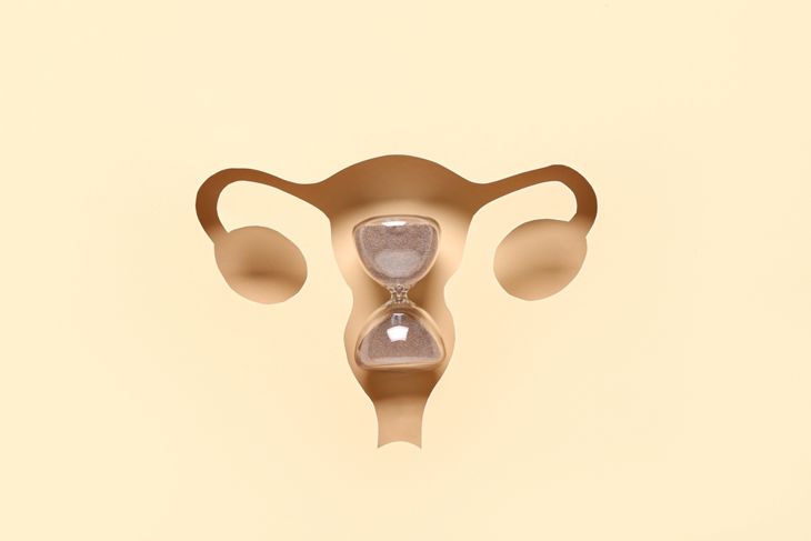 Hourglass visible through cut beige paper in shape of uterus, top view. Gynecology concept