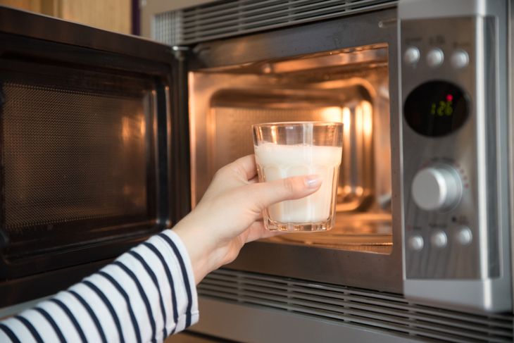 woman warming a glass of milk in the microwave