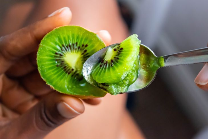 Kiwi fruit in hand. Girl eating ripe kiwi with tea dessert spoon.Summer fruit for healthy diet and vitamin C concept
