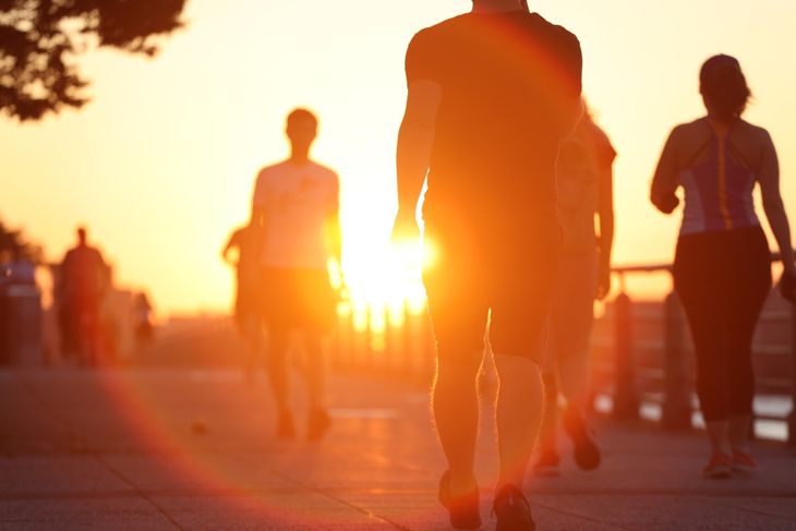 Group of unrecognized people exercise active walking on a riverside boardwalk at sunrise.