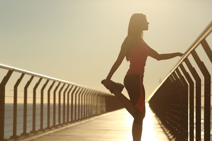 Runner silhouette doing stretching exercises at sunset in a bridge on the beach