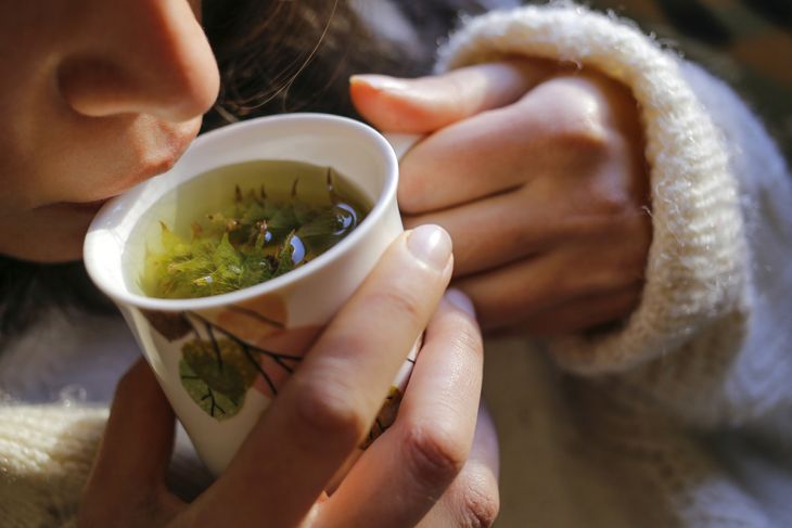 A young woman on the couch and with sage tea on the hand.