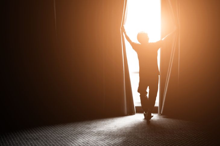 Man opening his bedroom blackout curtains 
