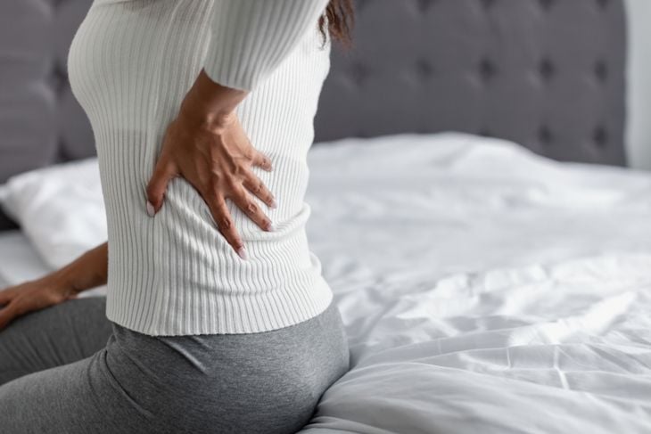 Coseup of a black woman sitting on the bed at home, touching lower back with hand