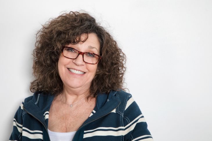 Happy mature woman studio portrait with active wear and glasses smiling, carefree at the camera.