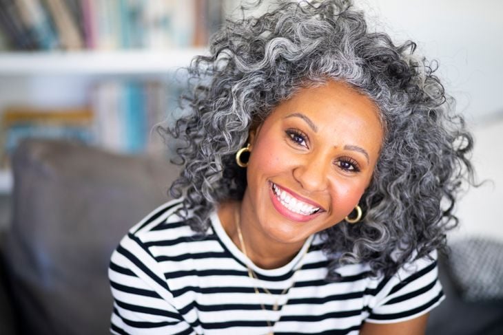 A beautiful black woman with white curly hair smiles for a headshot