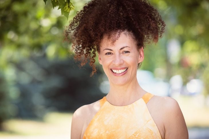Mature Ethnic Woman Smiling At The Camera. She is outside at the park. Hair in the air