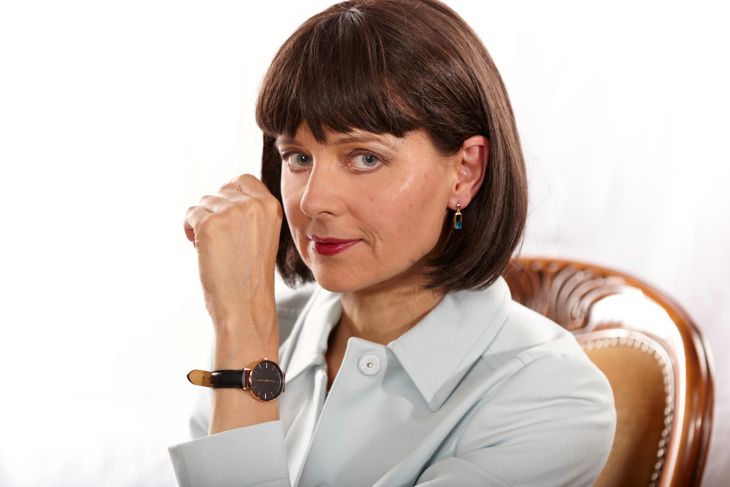 DSLR full frame image of a mature woman with brown hair wearing a an elegant green jacket and sitting on a french classic velvet provincial wooden upholstered dining chair with round backrest in Germany