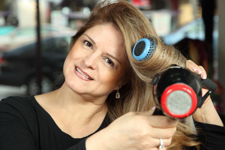 Woman blow drying long blond hair with a hair blower and brush slight smile and looking at camera. Image shot with Canon 5D, 100 ISO, 24-115mm lens, and studio strobes