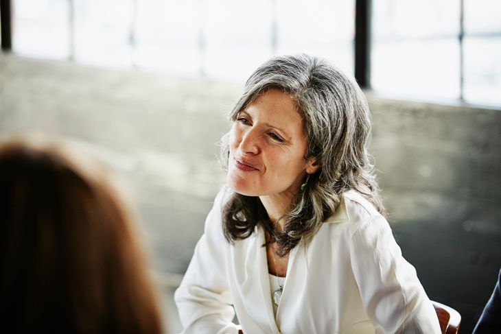 Smiling mature woman sitting at table with friends during dinner party