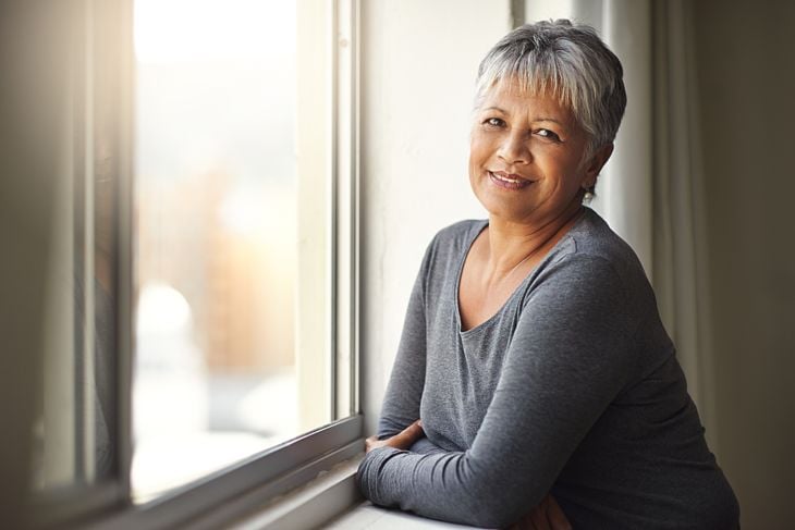 Shot of a mature woman standing by a window on a sunny day