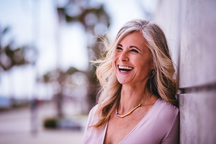 Candid portrait of attractive woman in her 60s laughing standing against wall in the city