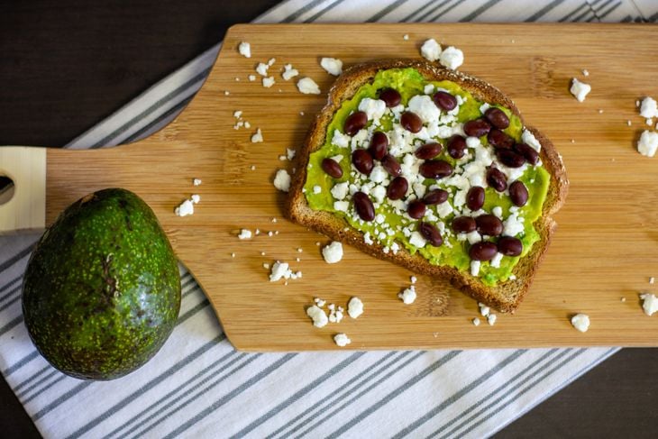 Overhead view of avocado toast with black beans and feta cheese on a wood cutting board