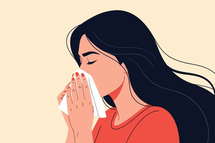 Young woman sneezing delicately into a white tissue