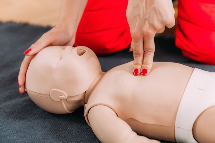 A close-up of an adult using two fingers to perform chest compressions on an infant CPR manikin, demonstrating the modified technique for providing CPR to infants. 