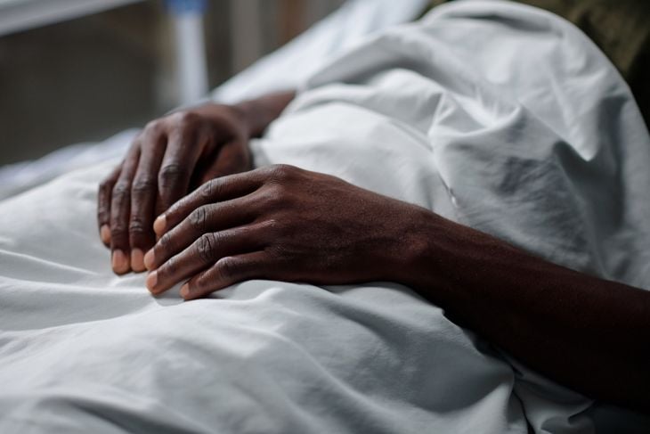 A close-up of a person’s hands resting on a white hospital blanket, conveying the critical condition and rapid decline that can occur in advanced PAM cases. 
