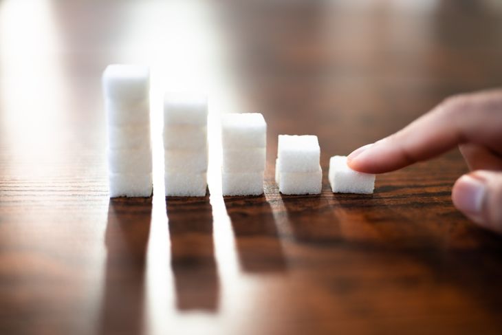 A hand points to a row of sugar cubes arranged in decreasing height on a wooden table, visually representing neem’s potential role in lowering blood sugar and supporting diabetes management. 