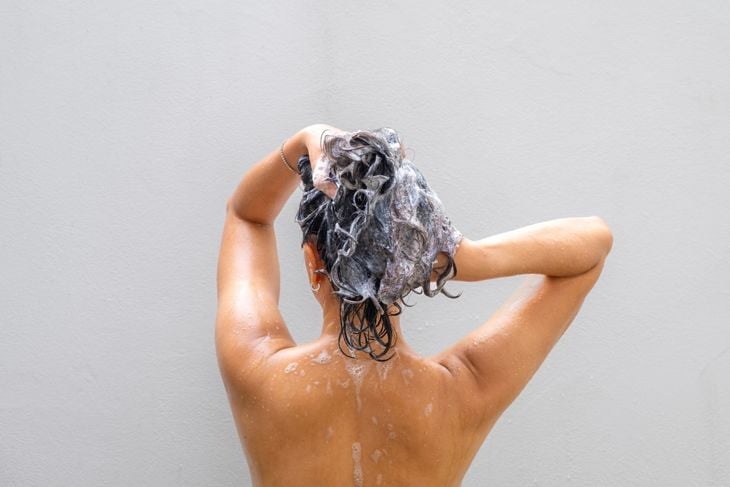 A person viewed from behind massages shampoo into their wet hair, illustrating that while neem is safe in topical products like shampoos, ingesting neem oil can be toxic and should be avoided without medical supervision. 