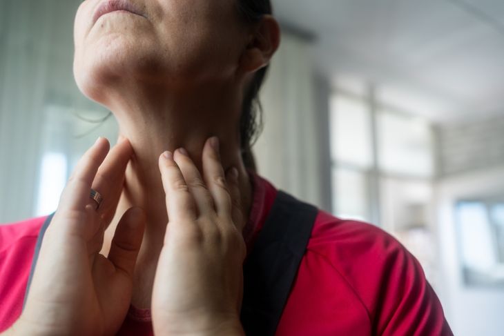A person in a pink top gently feels the sides of their neck, illustrating how thyroid nodules can develop in the lower neck and sometimes be detected by touch if they become large. 