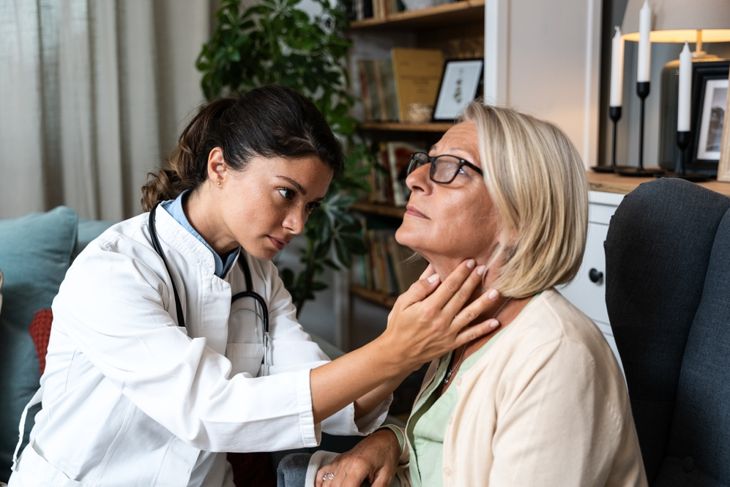 A doctor carefully examines an older woman’s neck with both hands during a checkup, highlighting the need for medical evaluation when a nodule changes, grows, or causes concerning symptoms. 