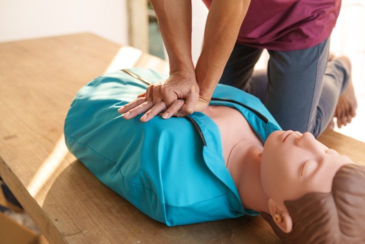 A person practicing chest compressions on a CPR training manikin dressed in a blue jacket, highlighting the importance of responding quickly to unresponsiveness or abnormal breathing. 