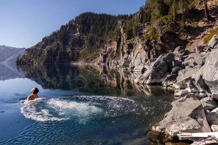 Man going in for a swim in Crater Lake NP Oregon in a beautiful calm afternoon, the Cleetwood Cove trail leads to the Shore and it is one of the only places where swimming in allowed.