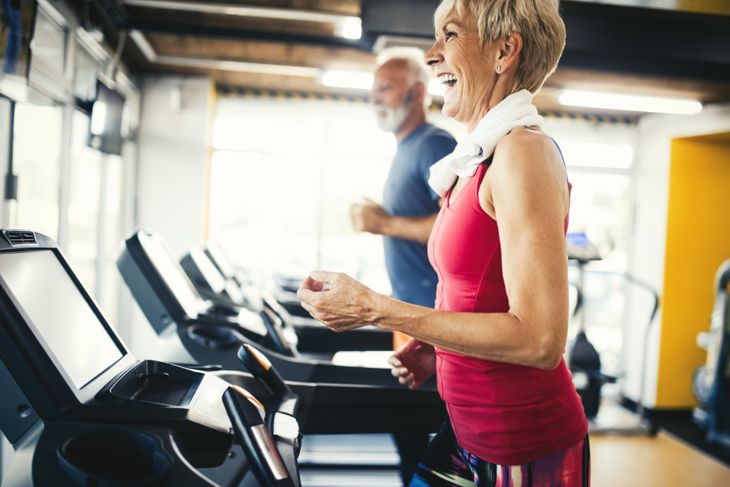 Older adults walking on treadmills in a bright gym, shown mid-stride and dressed in activewear. Their upright posture and engaged expressions suggest steady, intentional movement as part of a regular indoor fitness routine.