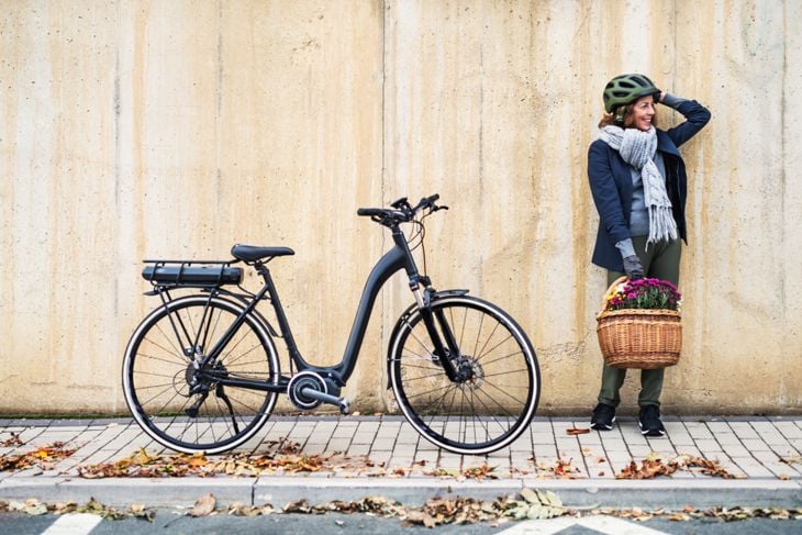 Active senior woman with electrobike standing outdoors