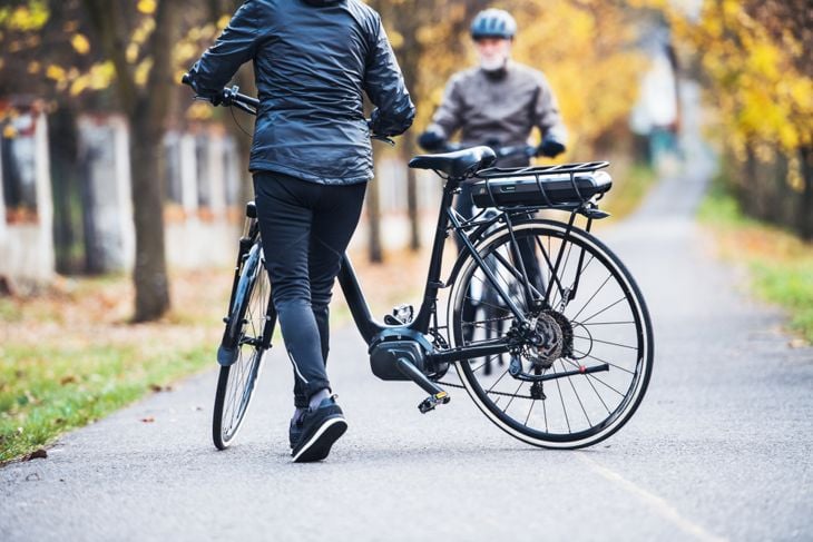 Active senior couple with electrobikes standing outdoors on a road in park.