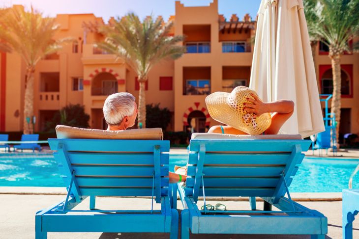 Senior couple relaxing by swimming pool lying on chaise-longues